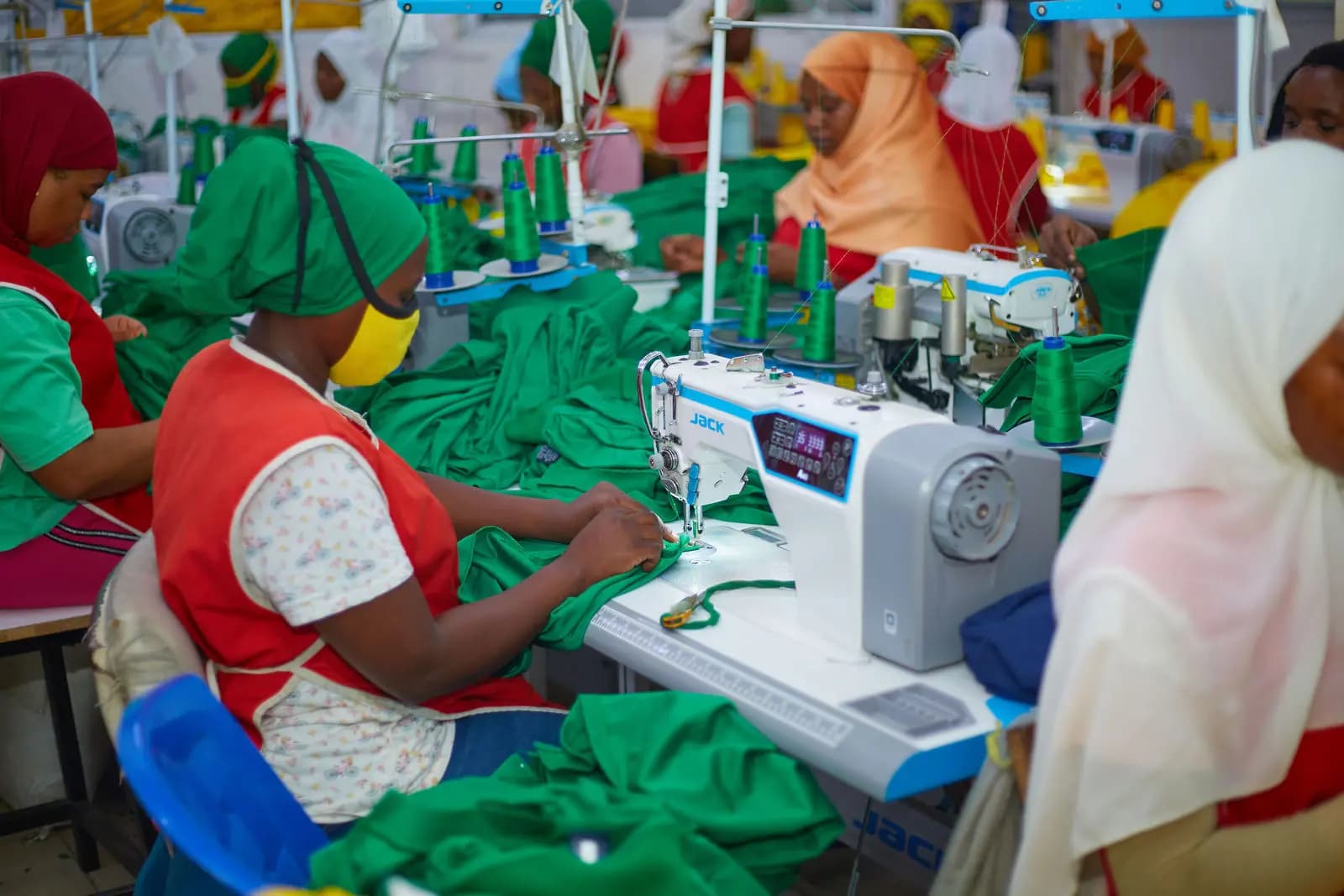 Washonaji wakishona nguo za kijani kwenye mstari Swahili Knits